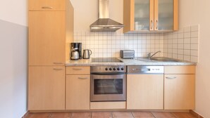 A compact kitchen with wooden cabinets, a stainless steel range hood, a built-in oven, a dishwasher, and a small countertop with a kettle and toaster. - Geraumiges Ferienhaus fur Familie im Hafendorf Muritz Rechlin (Rechlin)
