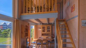 Interior de madera con comedor, escalera y vistas a través de amplios ventanales.