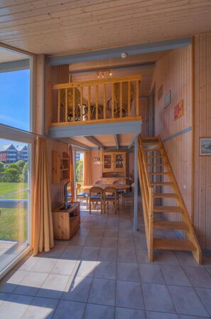 Ein Holzinnenraum mit Essbereich, einer Treppe und Blick durch große Fenster.
