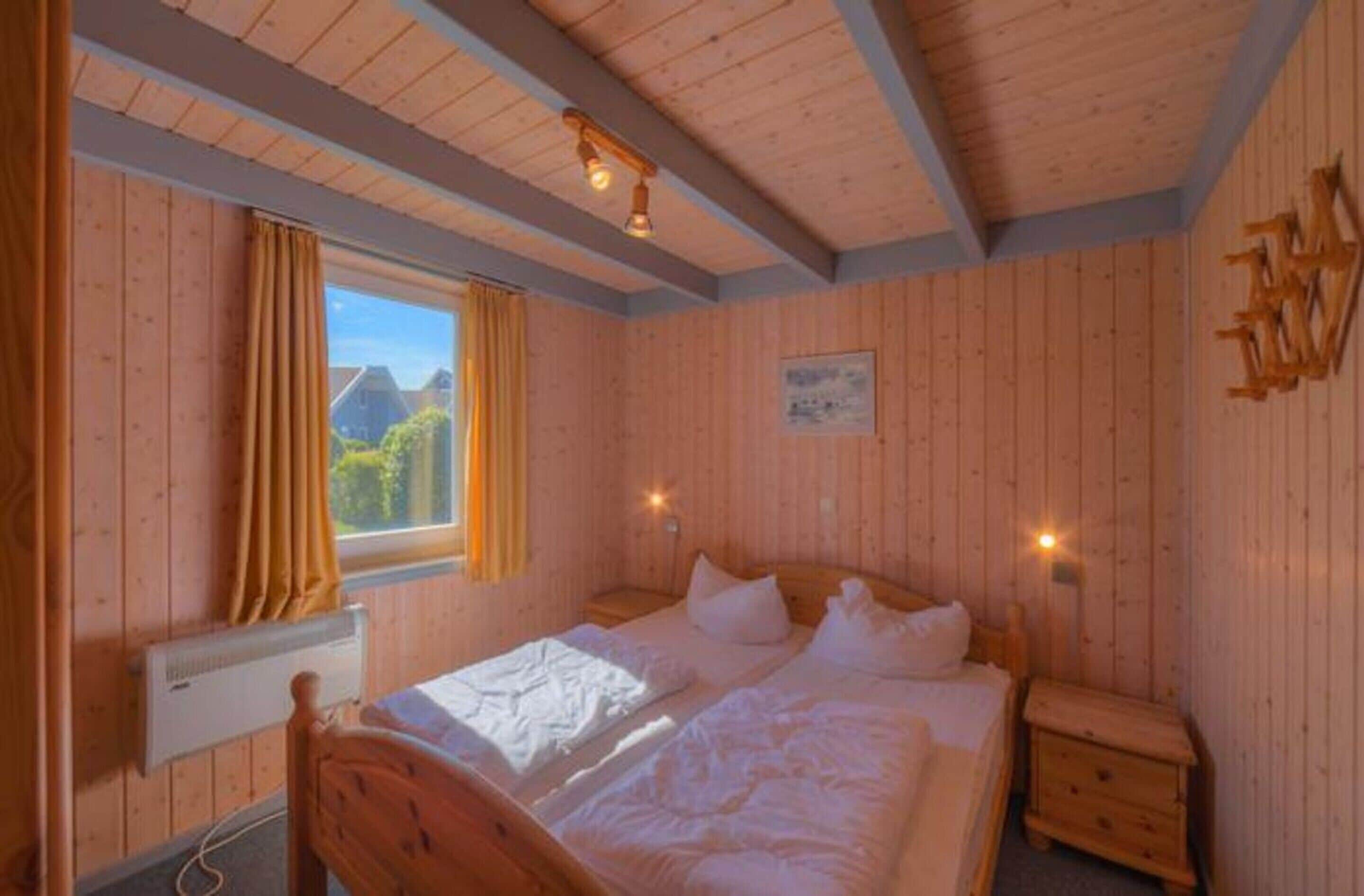 A wooden-paneled bedroom with a bed, two bedside tables, a window with curtains, and a radiator.