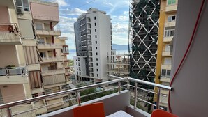 Un balcon avec une table et des chaises, donnant sur un paysage urbain avec des bâtiments et un ciel dégagé.