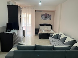 A hotel room with a bed, a sofa, a desk with a computer, a wardrobe, and a window with curtains. - Charming apartment in marvelous Vlorë (Vlorë)