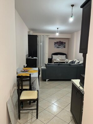 A compact room with a bed, a small table with chairs, a TV, and a ceiling light. - Charming apartment in marvelous Vlorë (Vlorë)