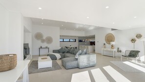 Ein modernes Wohnzimmer mit einem Ecksofa, einem Flachbildfernseher und einem Essbereich im Hintergrund.