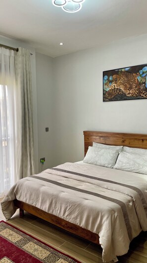 A bedroom with a wooden bed, a patterned rug, and a painting on the wall. - Think cozy loft living, open space, and floor-to-ceiling views of Lake Victoria. (Kampala)