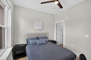 A bedroom with a bed, nightstands, a ceiling fan, a door, and a window. - Parkview Greer 2BR Retreat (Greer)