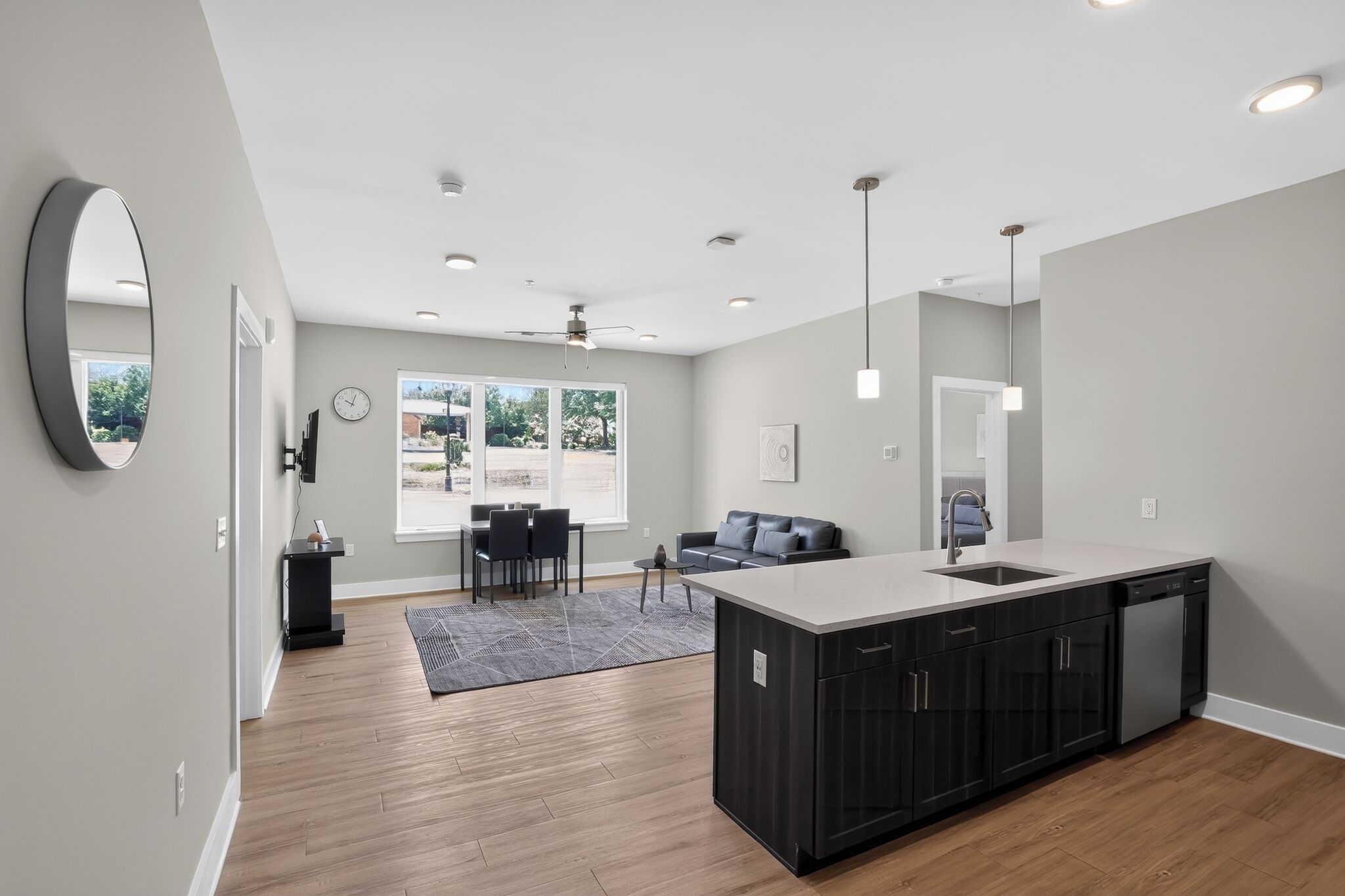 Een moderne keuken met een centraal eiland, een eetgedeelte met tafel en stoelen, en een groot raam dat voor daglicht zorgt.