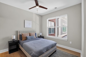A bedroom with a bed, nightstands, a ceiling fan, a window with a view, and a wall-mounted artwork. - Parkview Greer 2BR Getaway (Greer)