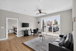 Ein modernes Wohnzimmer mit Deckenventilator, Essbereich und Balkon mit Stadtblick.
