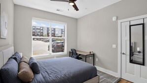 A bedroom with a bed, a desk, a chair, a ceiling fan, a window, and a door. - Homey 2BR with Great Space (Greer)