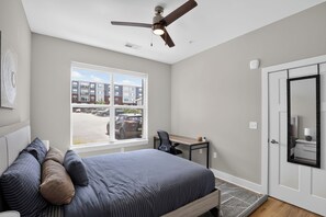 Ein Schlafzimmer mit Bett, Schreibtisch, Stuhl, Deckenventilator, Fenster und Tür.