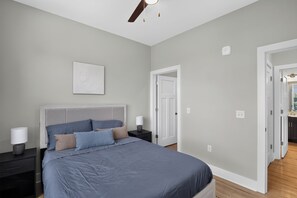Een slaapkamer met een bed, nachtkastjes, een plafondventilator en een deur naar een andere kamer.