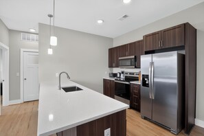 A modern kitchen with a central island, stainless steel appliances, and dark wooden cabinets. - Parkview Greer  2 Bedroom Haven (Greer)