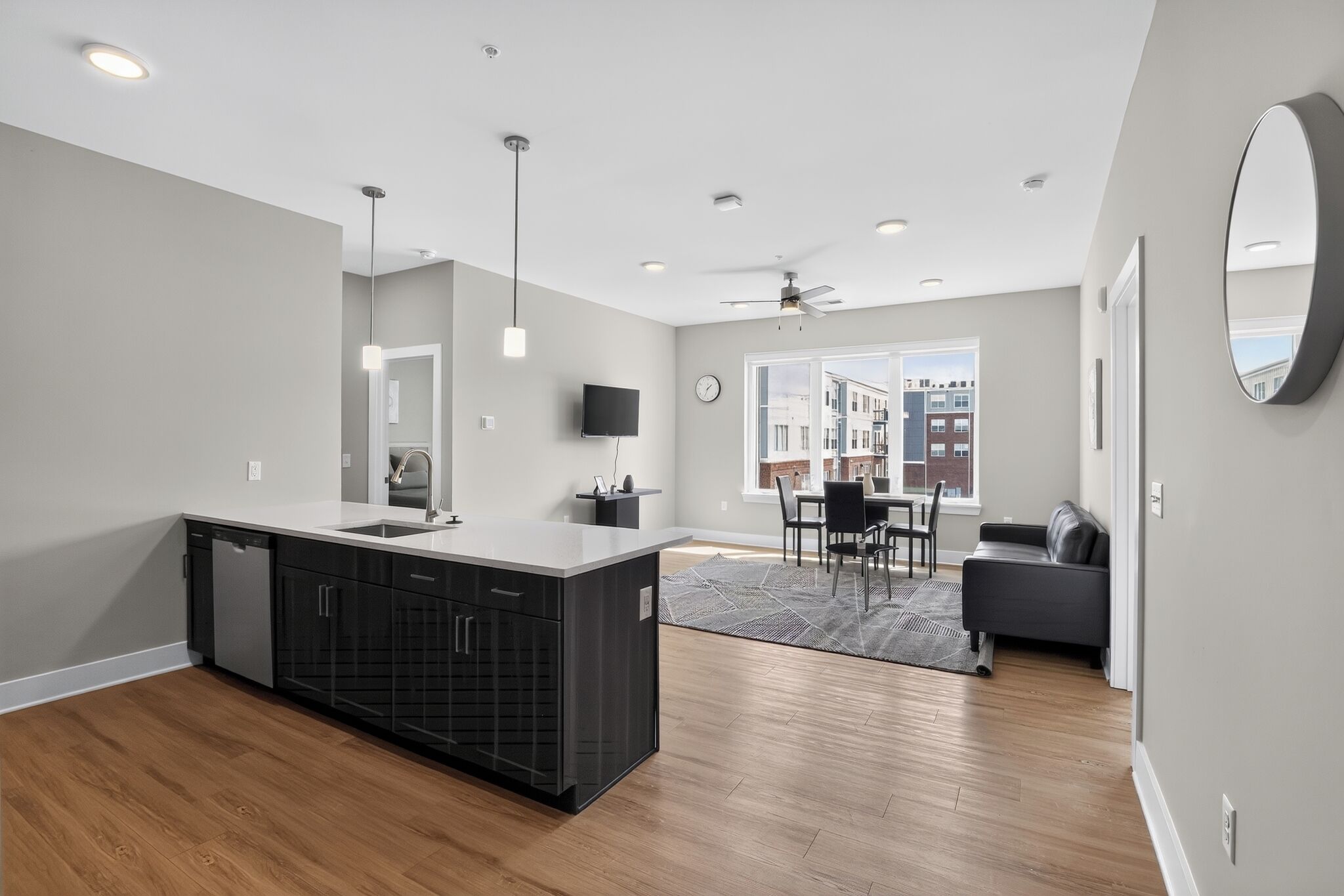 Una cocina moderna con una isla central, una zona de comedor con mesa y sillas, un sofá y un ventanal grande.