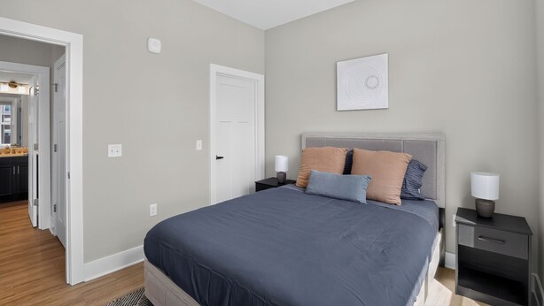 Un dormitorio con cama, mesitas de noche, ventilador de techo y una puerta que da a una cocina.