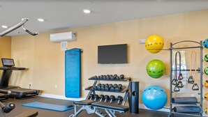 Un gimnasio con equipo de ejercicio, una cinta de correr y un televisor montado en la pared.