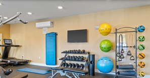 Ein Fitnessraum mit Trainingsgeräten, Laufband und Wandfernseher.