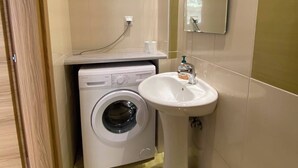 A compact bathroom with a washing machine, a sink, and a mirror.