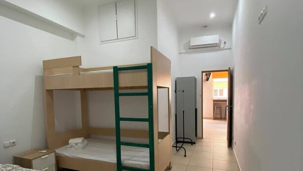A room with bunk beds, a desk, a chair, and a bed with a patterned bedspread.