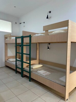 Dormitori amb lliteres, una escala, dues làmpades penjades a la paret i una finestra.