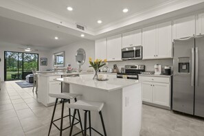 A modern kitchen with white cabinetry, stainless steel appliances, and a central island with bar stools.