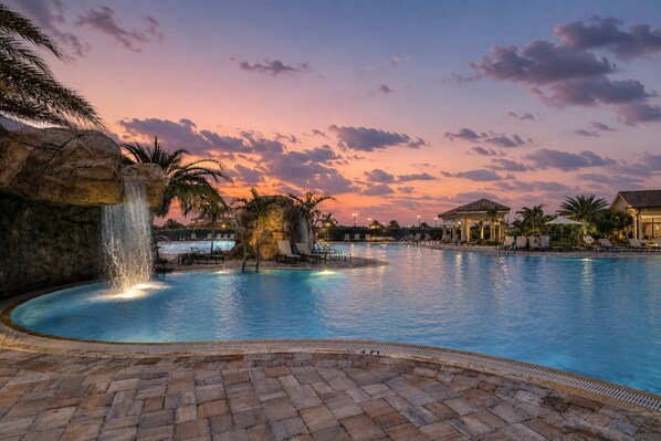 A pool with a waterfall feature, lounge chairs, and a gazebo.