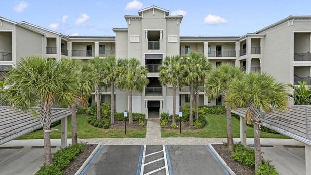 A multi-story residential building with a central entrance, surrounded by palm trees and a parking area. - New To Market- All New Furnishings- Lakewood National Golf Condo with Resort Amenities (Bradenton)