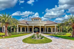 A large, two-story house with a circular central patio, surrounded by palm trees and a well-maintained lawn.