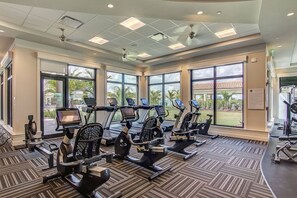 A gym with multiple cardio machines, large windows, and a view of a building outside.