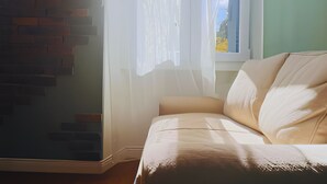 Ein Zimmer mit einem weißen Sofa, einem Fenster mit durchsichtigen Vorhängen und einer Ziegelwand.