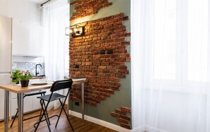 A kitchen with a brick wall, a dining table with chairs, and a potted plant. - Charming Liberty-Style Studio Apartment Near Milano Centrale, 10 Minutes Away (Milano)