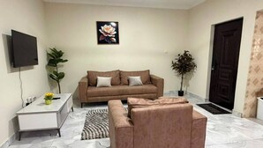 Una sala de estar con un sofá, una mesita, un televisor y dos plantas en macetas.