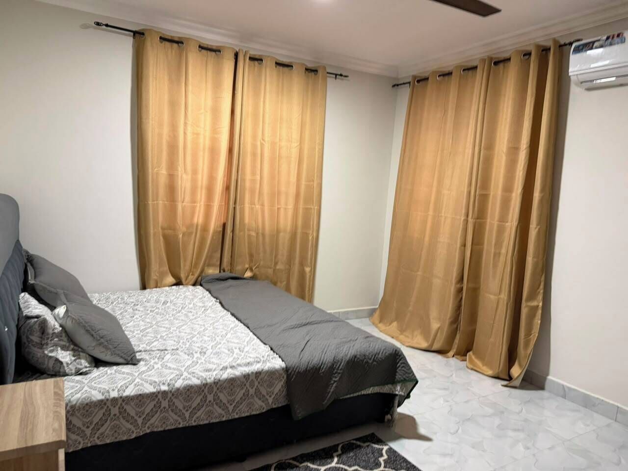 Een slaapkamer met een bed, gordijnen, een plafondventilator en een airconditioning.