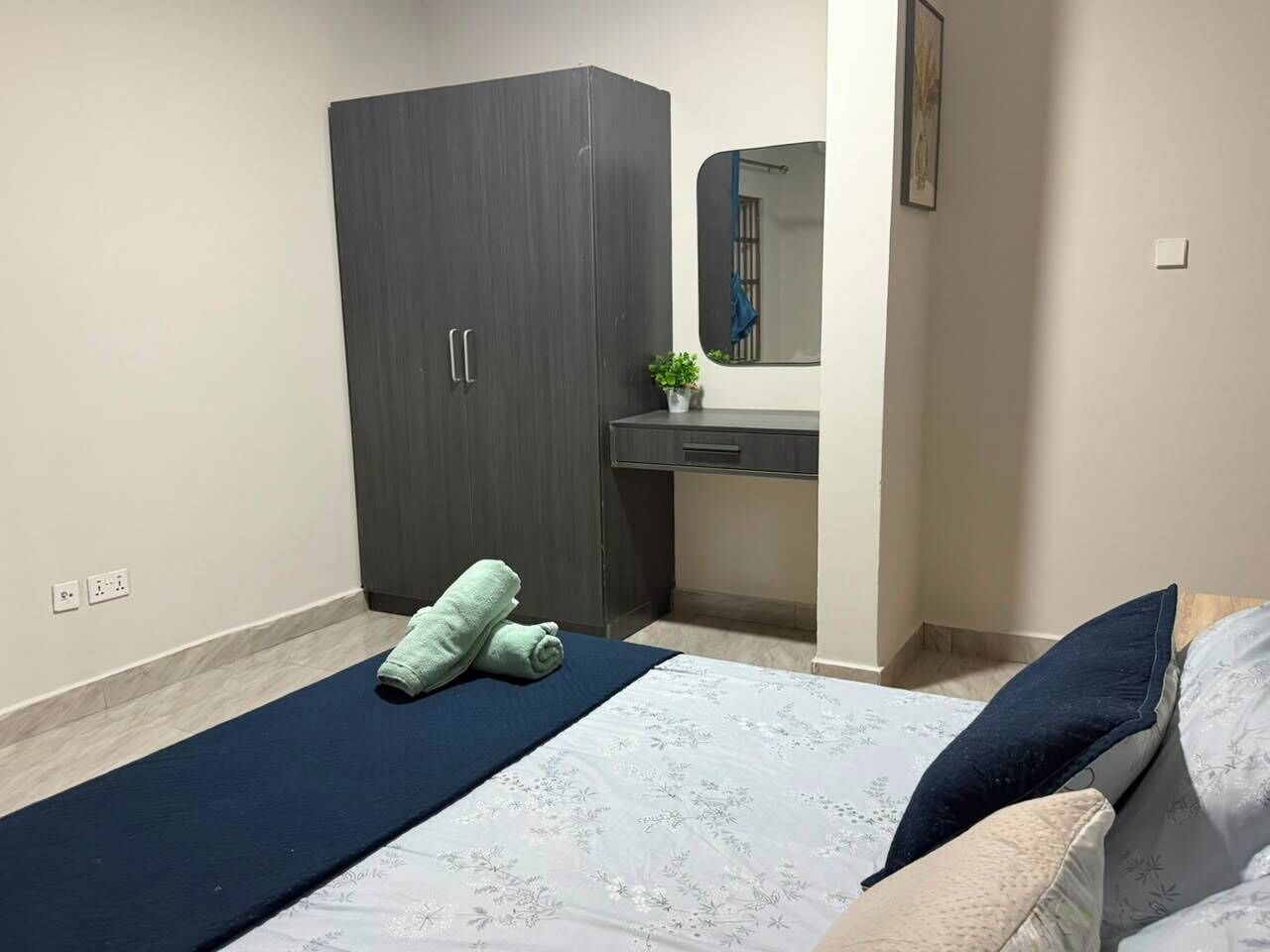 Een slaapkamer met een bed, een kledingkast, een nachtkastje met een plant en een spiegel.