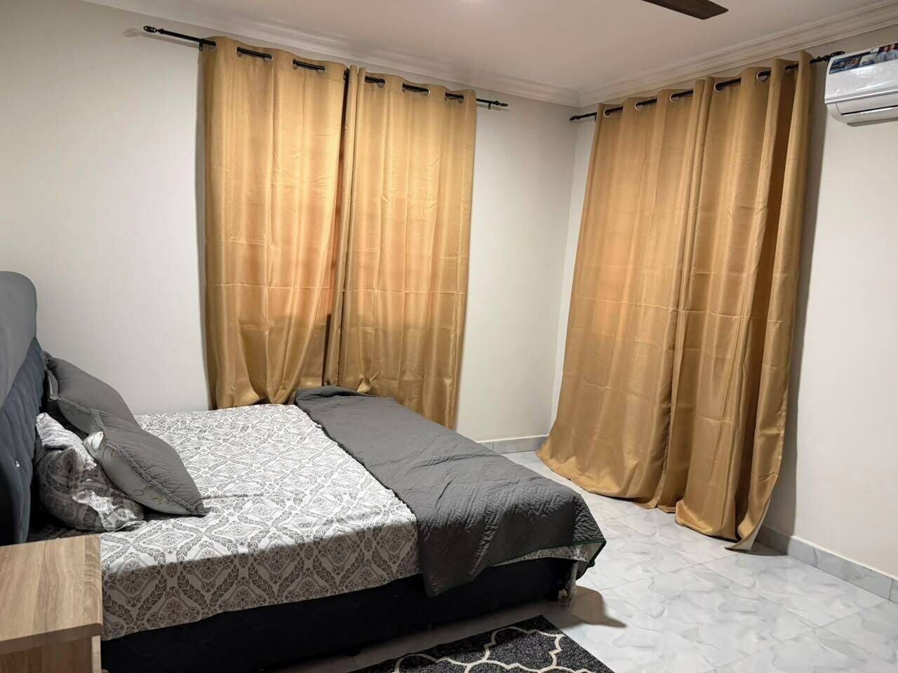 Quarto com cama, cortinas, ventoinha no teto e aparelho de ar condicionado.