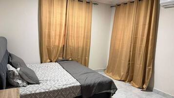 Quarto com cama, cortinas, ventoinha no teto e aparelho de ar condicionado.