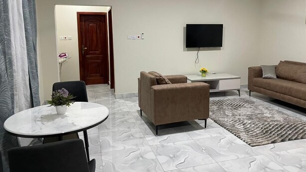 A living room with a sofa, a TV mounted on the wall, a ceiling fan, and a dining area with a table and chairs.