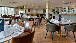 Un restaurant avec des tables rondes, des fauteuils en cuir et un coin bar.