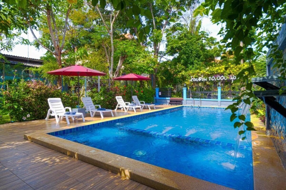 A swimming pool with lounge chairs and umbrellas, surrounded by greenery and a stone wall.