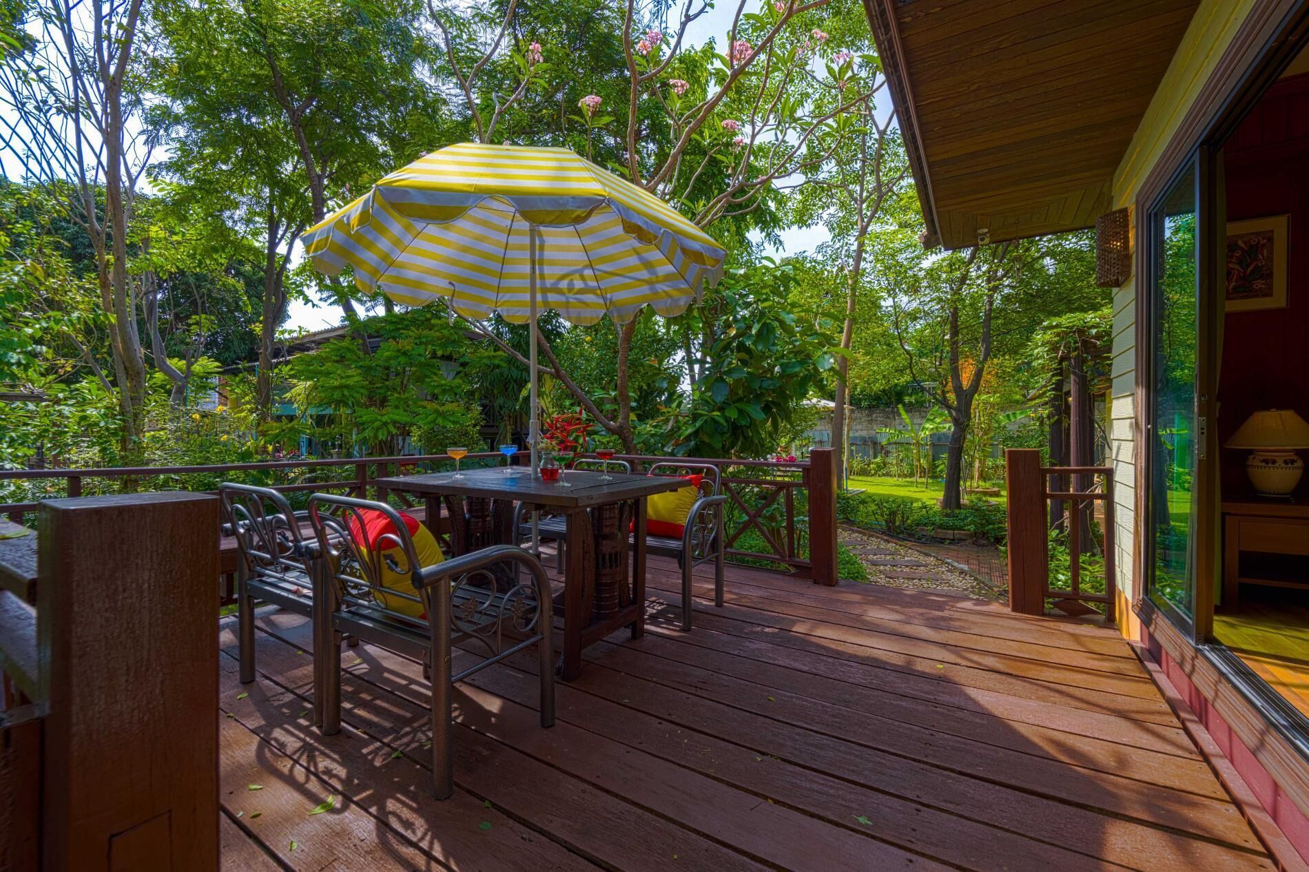 An outdoor patio with wooden flooring, metal chairs, a table, and a yellow-striped umbrella.
