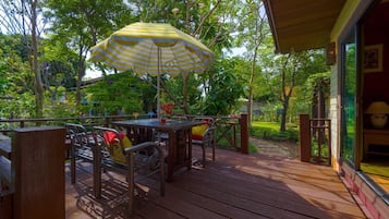 An outdoor patio with wooden flooring, metal chairs, a table, and a yellow-striped umbrella.
