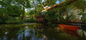 Un étang paisible où flotte un bateau en bois, entouré d’une végétation luxuriante et surplombé d’un pont traditionnel.