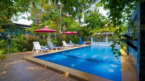 A swimming pool with lounge chairs and umbrellas, surrounded by greenery and a stone wall.