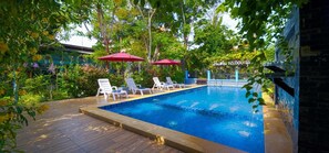 A swimming pool with lounge chairs and umbrellas, surrounded by greenery and a stone wall. - baansuanmuenbuppha (Hua Hin)