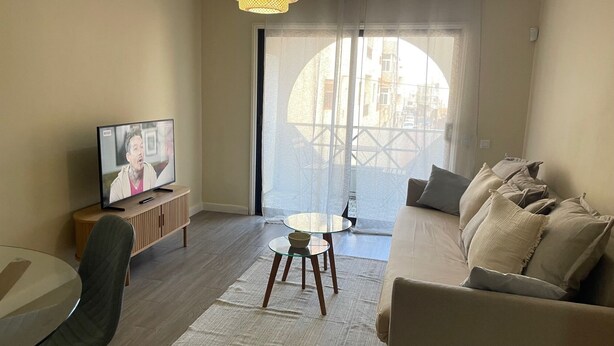 Ett vardagsrum med en tv, en soffa, ett glasbord och utsikt genom ett stort fönster.