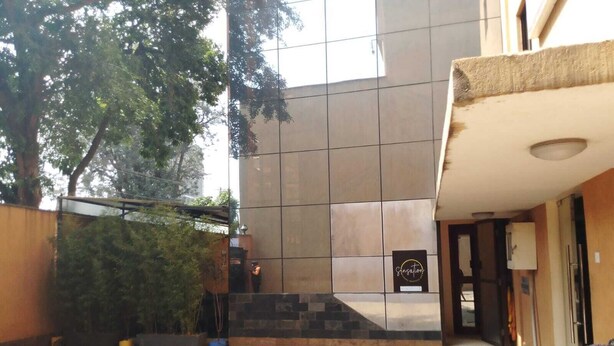 A modern building with a tiled facade, a visible entrance, and a person sitting outside. - Bar BnB Spa and Barber (Nairobi)