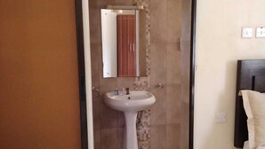 A hotel room with a sliding door leading to a bathroom, a white sink, and a mirror. - Bar BnB Spa and Barber (Nairobi)