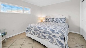Un dormitorio con cama, mesita de noche, lámpara y ventana.