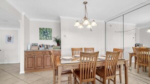 Un comedor con mesa y sillas de madera, una lámpara de araña y una zona de cocina con armarios y encimera.