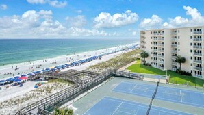 Una propiedad frente a la playa con cancha de tenis, sombrillas y un edificio con balcones.